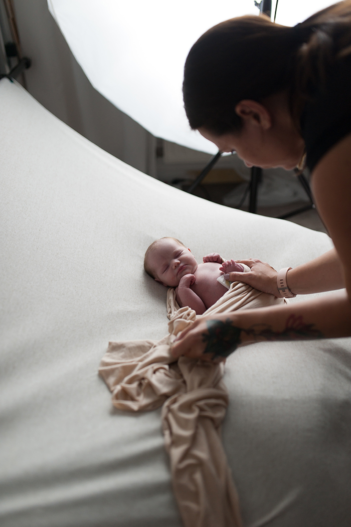 Photographe nouveau-né en train de poser un nouveau-né grâce à un wrap pour des images artistiques et un bébé calme et apaisé.