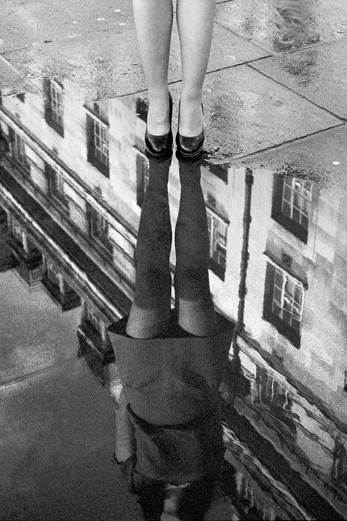 Photo de rue, en argentique, d'une jeune femme et son reflet dans une flaque d'eau. Par Gildas Lepetit-castel