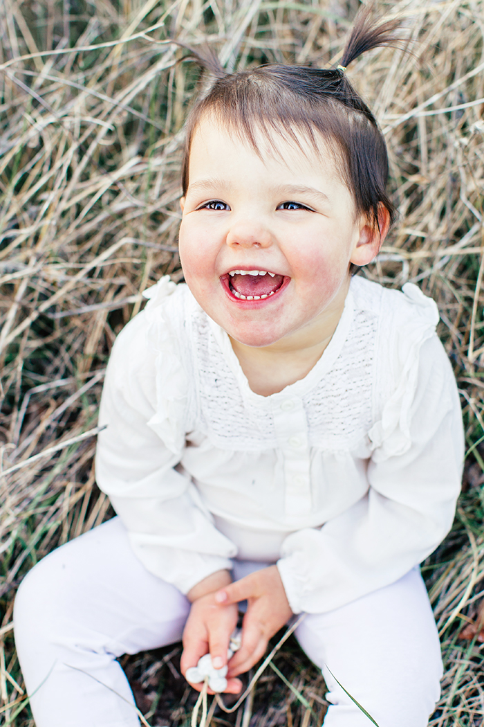 Portrait d'une petite fille qui rigole, vétue de blanc comme pour un baptême.