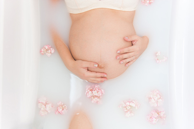 Photo de grossesse dans un bain de lait, entouré de jolies fleurs. Une photo romantique et artistique.